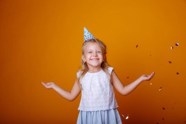 Stüdyoda turuncu arka planda poz veren sevimli doğum günü kızı.