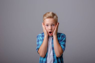 Gri arka plandaki bir çocuk duygularını, kızgınlığını, neşesini, şaşkınlığını gösterir.