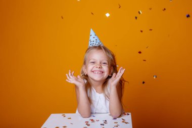 Stüdyoda turuncu arka planda poz veren sevimli doğum günü kızı.