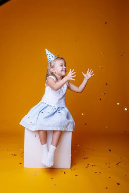 Doğum günü kızı stüdyoda turuncuya karşı oturuyor.