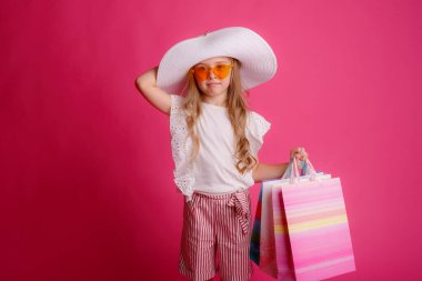 Bir sürü alışveriş çantası, güneş gözlüğü ve şapka takan şık küçük bir kız.  