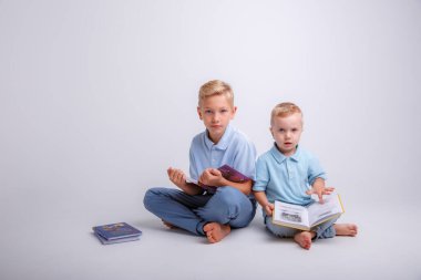 İki küçük çocuk yerde oturup kitap okuyorlar.