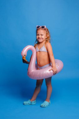 Mavi arka planda, mayolu ve güneş gözlüklü küçük kız.