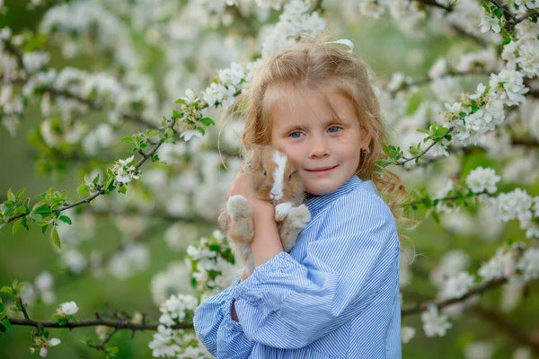 Una Niña Sostiene Conejo Sus Manos Árbol Floreciente Primavera — Foto de Stock