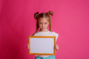 Boş bir çerçeve tutan bir kızın portresi, pembe bir arka planda, metin için yer 