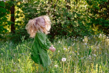 Sarışın kız karahindiba dolu tarlada poz veriyor.