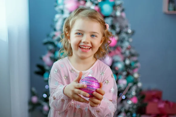Una Bambina Vicino All Albero Natale Che Tiene Una Bagattella — Foto Stock