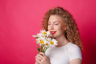 Kıvırcık kız pembe arka planda bir buket papatya tutuyor. 
