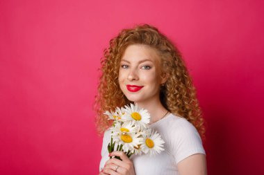 Kıvırcık kız pembe arka planda bir buket papatya tutuyor. 