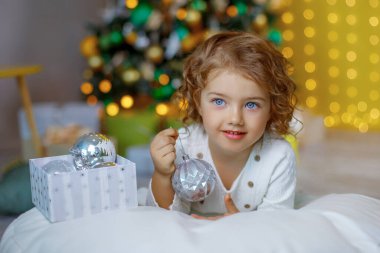 Gümüş mücevherlerle dolu bir kutuyla Noel ağacının yanında küçük bir kız 