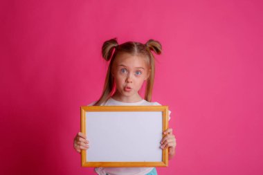 Boş bir çerçeve tutan bir kızın portresi, pembe bir arka planda, metin için yer 