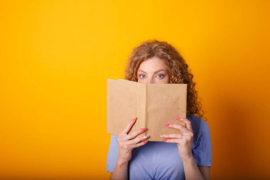 Güzel bir kadın kitap ile turuncu arka planda poz veriyor