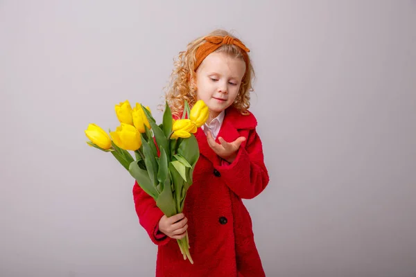 一个小孩 一个金发碧眼的女孩 手里拿着一束灰色背景的黄色郁金香 — 图库照片