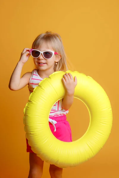 Sarı Arka Planda Şişirilebilir Yüzüğü Olan Güneş Gözlüklü Küçük Kız — Stok fotoğraf