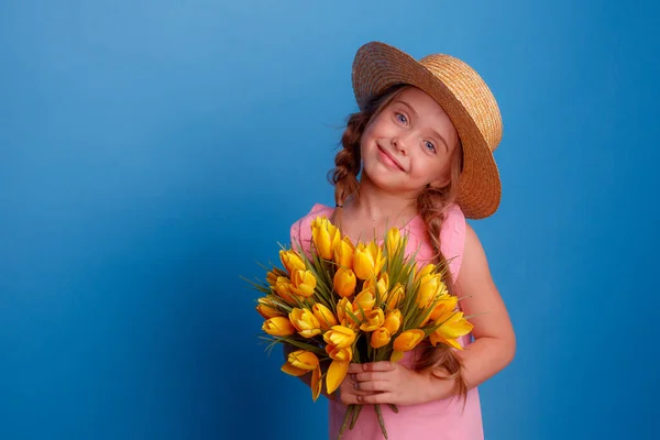 Malá Dívka Slaměném Klobouku Drží Kytici Žlutých Tulipánů Modrém Pozadí — Stock fotografie