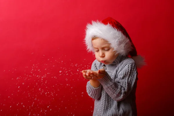 Ragazzo Con Cappello Babbo Natale Soffia Neve Uno Sfondo Rosso — Foto Stock