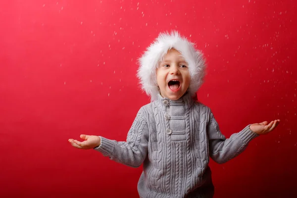 Ragazzo Con Cappello Babbo Natale Cattura Neve Uno Sfondo Rosso — Foto Stock