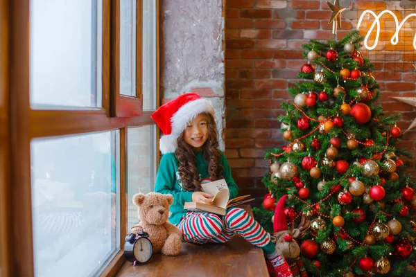 Little Asian Girl Pajamas Sitting Window Christmas Tree Reading Book — Stock Photo, Image