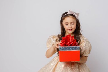 Güzel elbiseli küçük bir kız beyaz arka planda bir hediye kutusu tutuyor.