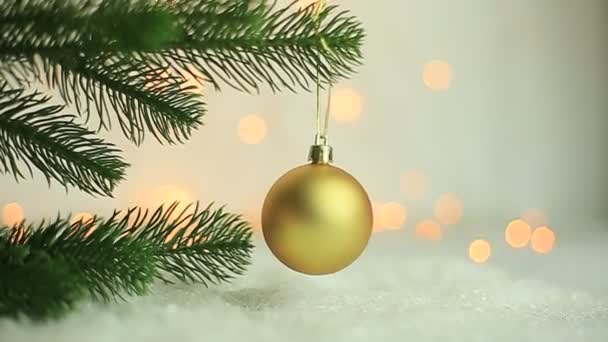 De kerstboom met een gelukkig nieuwjaar is versierd met een gouden glazen bal op een tak tegen een achtergrond van flikkerende zijgloeilampen, bloemenslingers voor een familievakantie. Feestelijke stemming. Positieve emotie — Stockvideo