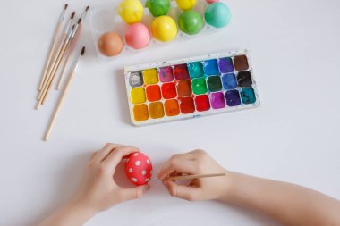 Bir çocuğun elleri beyaz arka planda bir Paskalya yumurtası süsler.