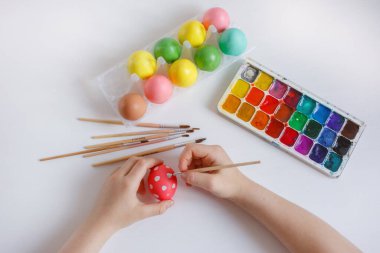 Bir çocuğun elleri beyaz arka planda bir Paskalya yumurtası süsler.