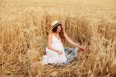 Hamile kadın buğday tarlasında, battaniyenin üzerinde oturuyor.