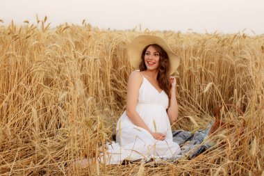 Hamile kadın buğday tarlasında, battaniyenin üzerinde oturuyor.