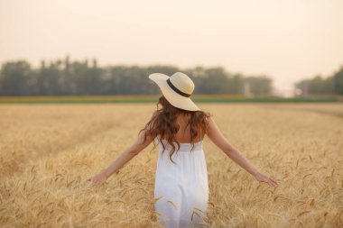Genç bir kadın sırtı buğday tarlasına dönük duruyor.