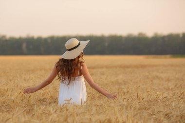 Genç bir kadın sırtı buğday tarlasına dönük duruyor.