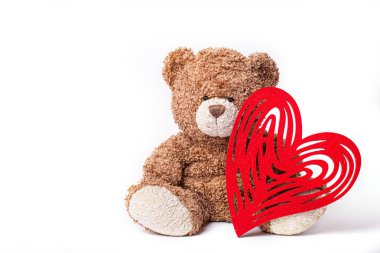 Beyaz arka plandaki oyuncak ayıcık Sevgililer Günü için bir kalp taşıyor