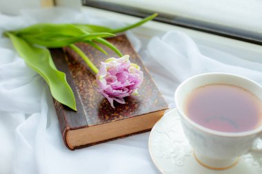 Bir kupa çay eski bir kitap bir buket lale pencerenin üzerinde