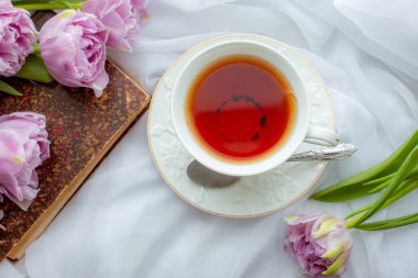 Bir kupa çay eski bir kitap bir buket lale pencerenin üzerinde