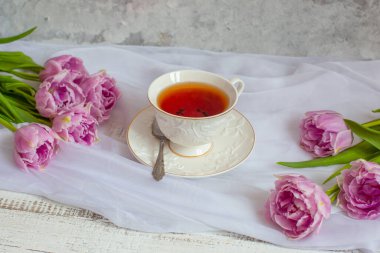 Hayat dolu çay fincanı ve bir buket lale beyazı kumaş.