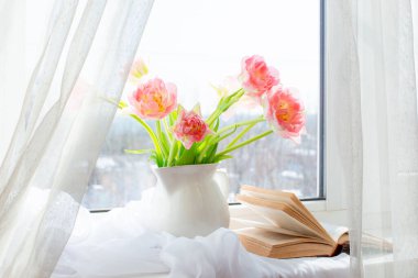 Hayat laleli bir vazo ve penceresinde eski bir kitap.