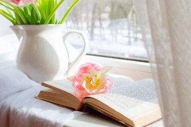 Hayat laleli bir vazo ve penceresinde eski bir kitap.