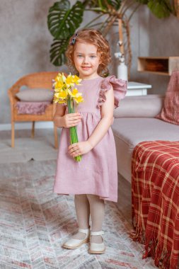 Küçük tatlı kız elinde bir buket nergis tutuyor.