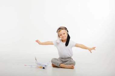 Pilot şapkalı küçük bir çocuk ve beyaz bir arka planı olan bir uçak.