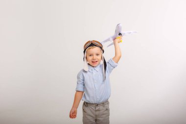 Pilot şapkalı küçük bir çocuk ve beyaz bir arka planı olan bir uçak.