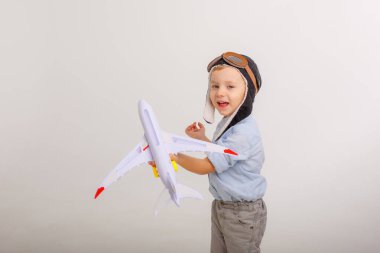 Pilot şapkalı küçük bir çocuk ve beyaz bir arka planı olan bir uçak.