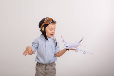Pilot şapkalı küçük bir çocuk ve beyaz bir arka planı olan bir uçak.
