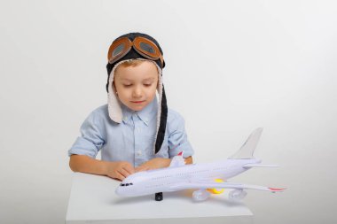 Pilot şapkalı küçük bir çocuk ve beyaz bir arka planı olan bir uçak.