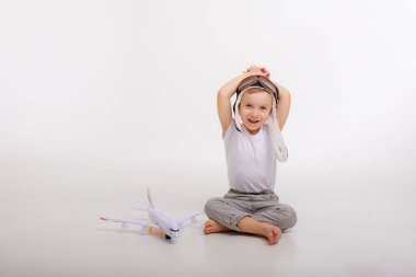 Pilot şapkalı küçük bir çocuk ve beyaz bir arka planı olan bir uçak.