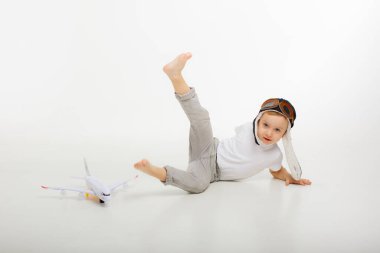 Pilot şapkalı küçük bir çocuk ve beyaz bir arka planı olan bir uçak.