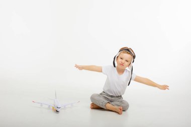 Pilot şapkalı küçük bir çocuk ve beyaz bir arka planı olan bir uçak.