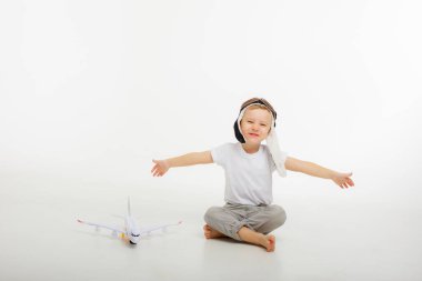 Pilot şapkalı küçük bir çocuk ve beyaz bir arka planı olan bir uçak.