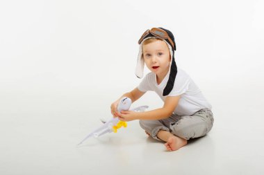 Pilot şapkalı küçük bir çocuk ve beyaz bir arka planı olan bir uçak.