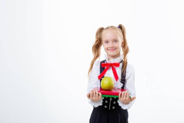 Okul üniformalı küçük bir kız beyaz bir arka planda kitap ve elma tutuyor.