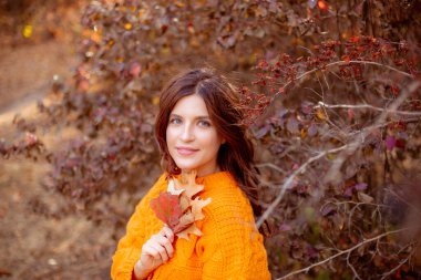 Sonbahar parkında turuncu kazaklı genç bir kadın.