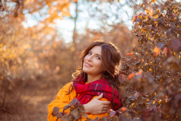 一位穿着橙色毛衣的年轻女子在秋天的公园里披着围巾 — 图库照片